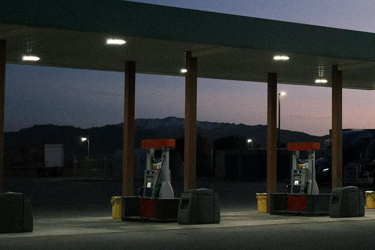 Fuel dispensers under a lit canopy at dusk, with desert mountains behind — gas station and convenience store insurance.